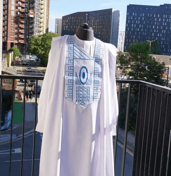 White Agbada with blue geometric embroidery, photographed on a balcony above the city